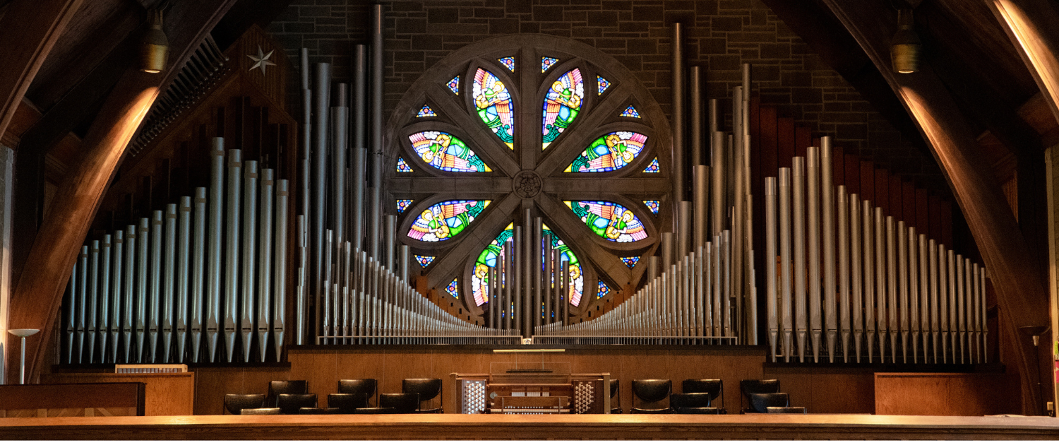 A colorful stained glass window surrounded by organ pipes. Superimposed text reading "Worship with us in-person or online every Sunday at 10:30AM Central Time. Click here for instructions on how to access the worship livestream."